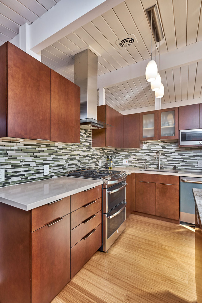 Classic l-shaped kitchen/diner in San Francisco with a single-bowl sink, flat-panel cabinets, medium wood cabinets, engineered stone countertops, green splashback, glass tiled splashback, stainless steel appliances, bamboo flooring and an island.
