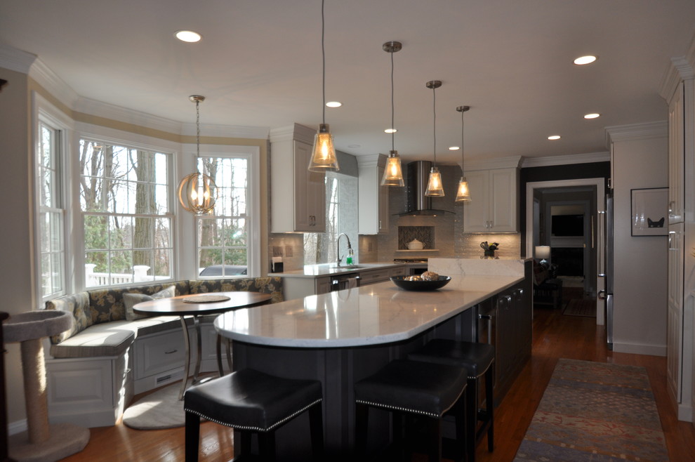 This is an example of a medium sized classic l-shaped open plan kitchen in Boston with a submerged sink, raised-panel cabinets, white cabinets, engineered stone countertops, grey splashback, porcelain splashback, stainless steel appliances, medium hardwood flooring, an island, brown floors and white worktops.