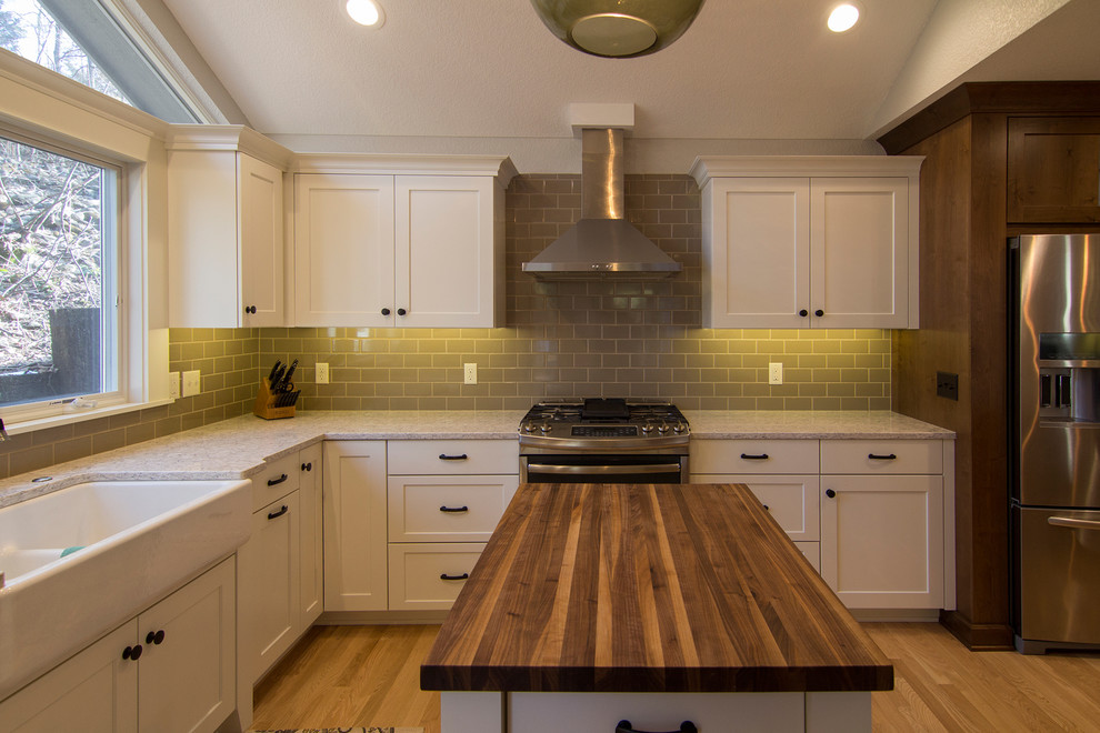 Example of a large transitional l-shaped light wood floor eat-in kitchen design in Milwaukee with a farmhouse sink, shaker cabinets, white cabinets, quartz countertops, gray backsplash, subway tile backsplash, stainless steel appliances and an island