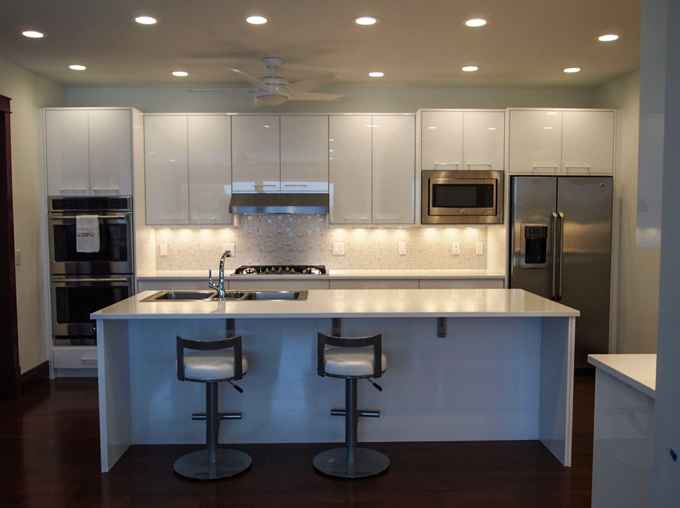 Modern inredning av ett stort kök, med en nedsänkt diskho, släta luckor, vita skåp och en köksö
