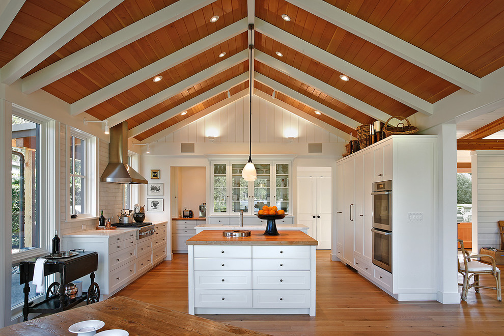 Eat-in kitchen - mid-sized transitional u-shaped medium tone wood floor eat-in kitchen idea in Seattle with flat-panel cabinets, white cabinets, wood countertops, white backsplash, ceramic backsplash, stainless steel appliances and an island