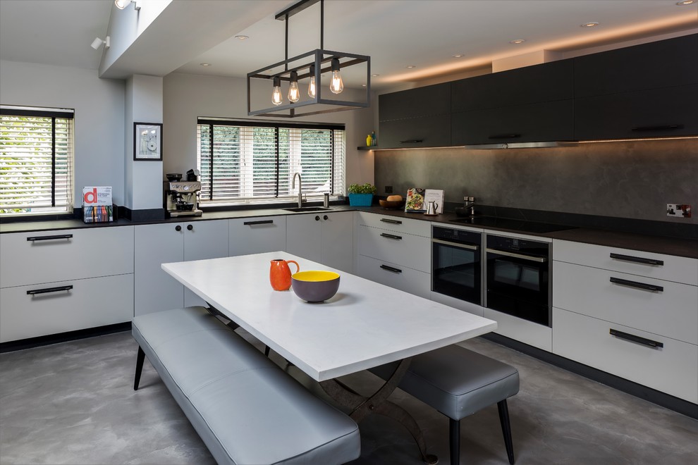 Design ideas for a medium sized contemporary l-shaped kitchen/diner in London with flat-panel cabinets, a single-bowl sink, grey splashback, black appliances, concrete flooring, grey floors and black worktops.