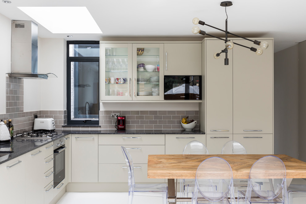 Example of a mid-sized trendy white floor open concept kitchen design in London with an undermount sink, flat-panel cabinets, beige cabinets, gray backsplash, subway tile backsplash and no island