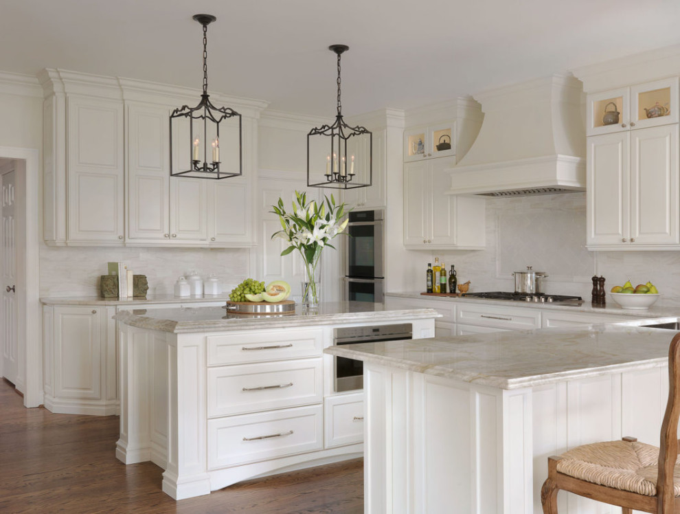 Inspiration for a traditional l-shaped kitchen in Chicago with raised-panel cabinets, white cabinets, white splashback, stainless steel appliances, medium hardwood flooring, multiple islands and beige worktops.