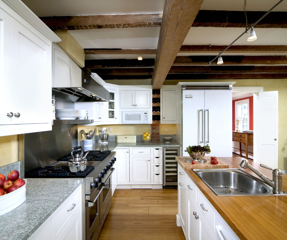 Modelo de cocina clásica con electrodomésticos blancos, encimera de madera, fregadero encastrado, armarios con rebordes decorativos y puertas de armario blancas