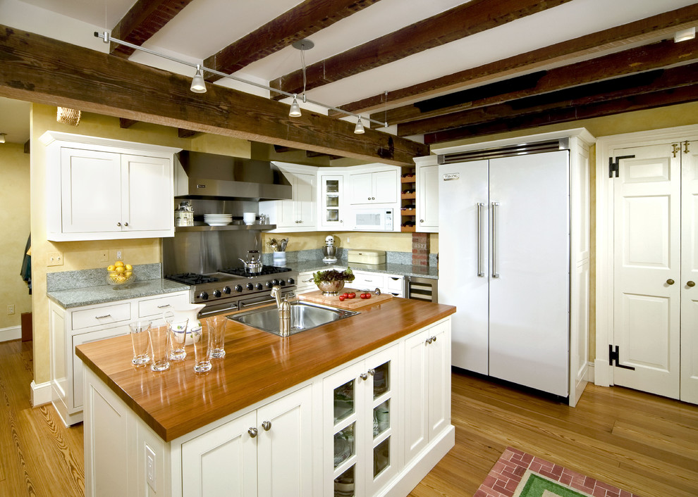 Foto på ett vintage kök, med luckor med infälld panel, träbänkskiva, en nedsänkt diskho, vita skåp och vita vitvaror