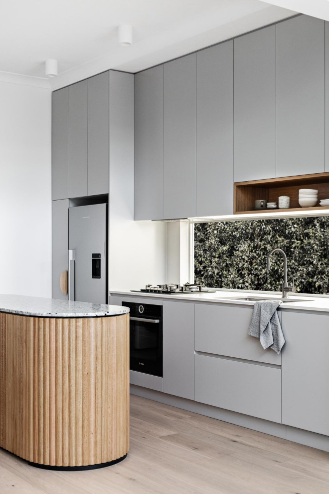Modern inredning av ett litet grå grått kök, med en dubbel diskho, grå skåp, bänkskiva i terrazo, svarta vitvaror, ljust trägolv och en köksö