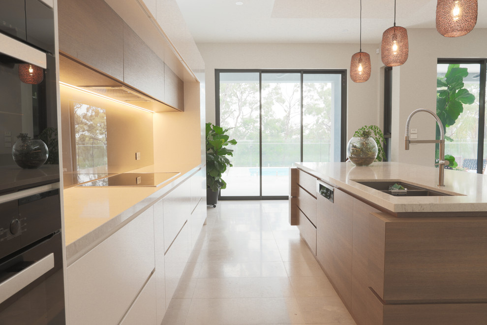 Inspiration for an expansive contemporary galley open plan kitchen in Sydney with a submerged sink, flat-panel cabinets, white cabinets, engineered stone countertops, brown splashback, glass sheet splashback, black appliances, ceramic flooring, an island, grey floors and white worktops.