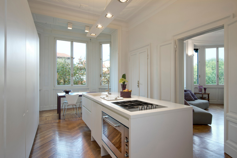 Immagine di una cucina design di medie dimensioni con lavello integrato, ante lisce, ante bianche, top in superficie solida, elettrodomestici in acciaio inossidabile e pavimento in legno massello medio