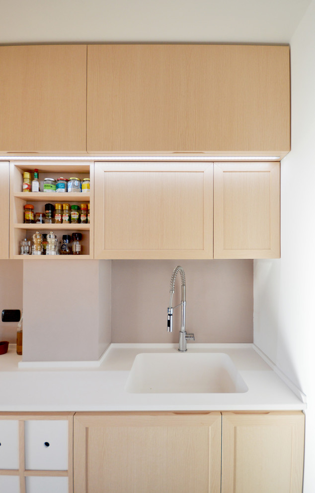 Diseño de cocina lineal actual con puertas de armario de madera clara, península, fregadero integrado, armarios con paneles empotrados y encimera de acrílico