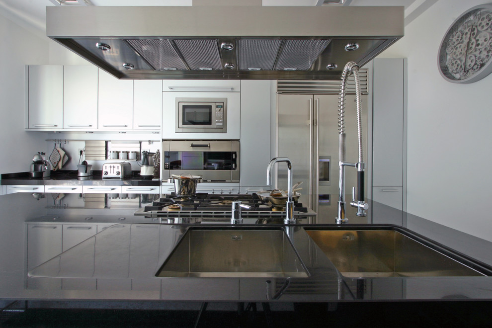 Foto på ett stort industriellt linjärt kök, med en undermonterad diskho, släta luckor, vita skåp, rostfria vitvaror och en köksö