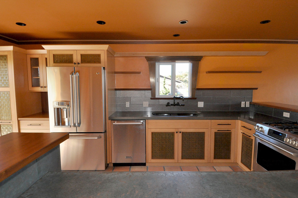 Bild på ett mellanstort maritimt kök, med en undermonterad diskho, skåp i shakerstil, skåp i ljust trä, bänkskiva i betong, stänkskydd med metallisk yta, stänkskydd i porslinskakel, rostfria vitvaror, klinkergolv i terrakotta, en halv köksö och rött golv