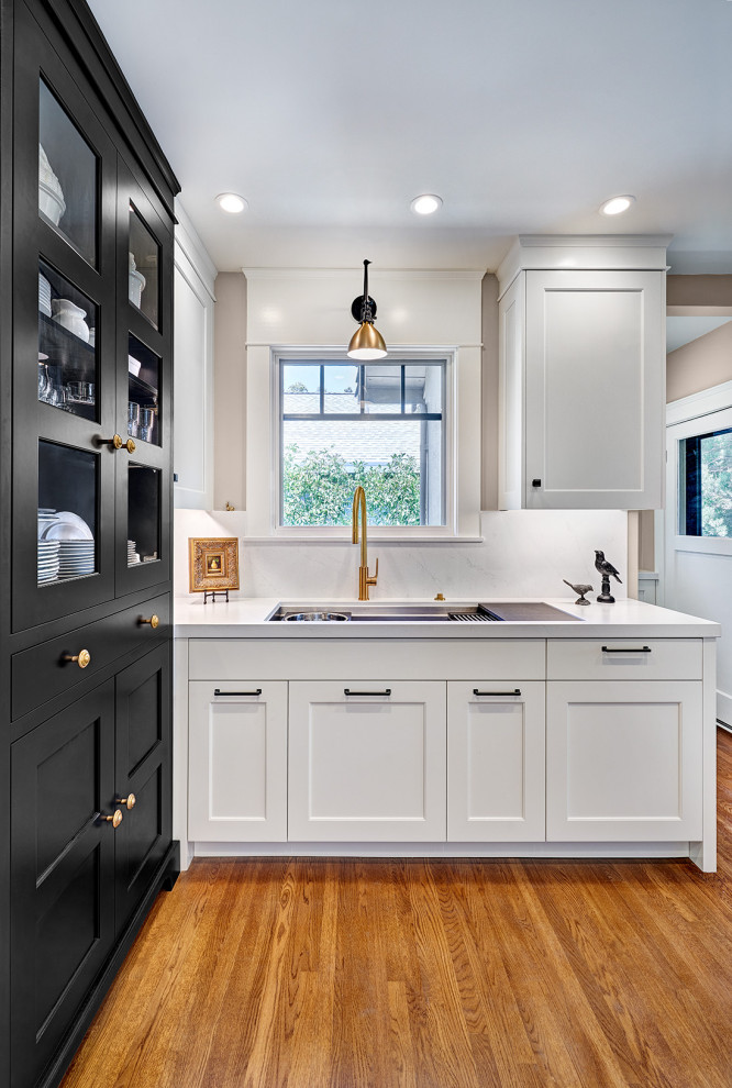 Foto på ett litet amerikanskt vit kök, med en undermonterad diskho, skåp i shakerstil, svarta skåp, bänkskiva i kvarts, vitt stänkskydd, integrerade vitvaror, mellanmörkt trägolv och flerfärgat golv
