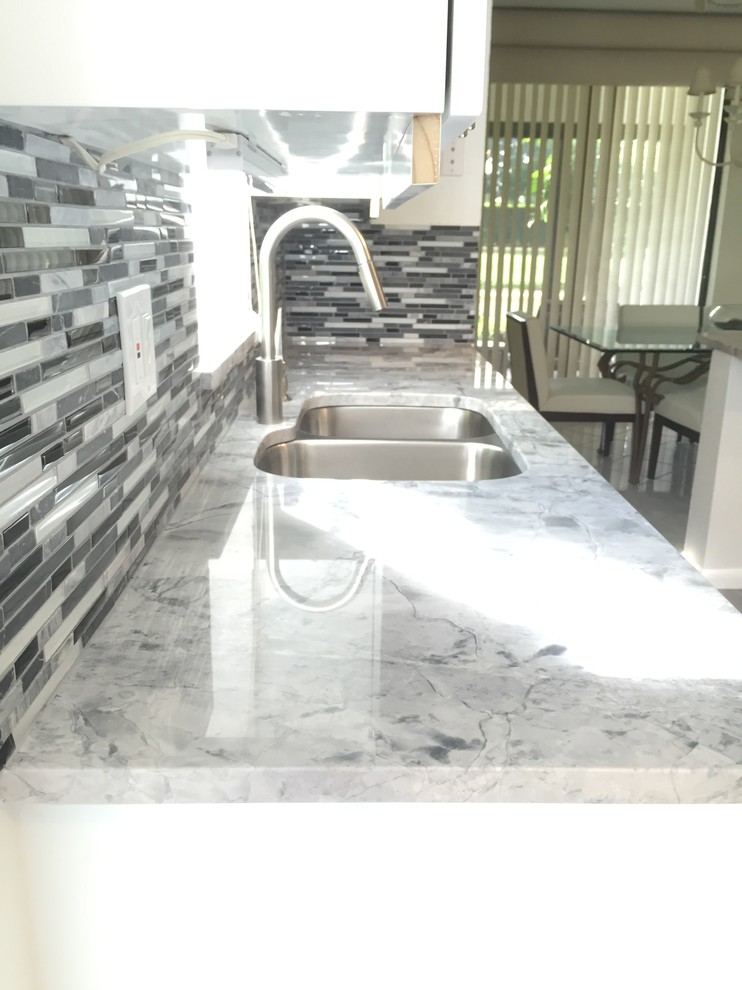 Modern inredning av ett mellanstort kök, med en undermonterad diskho, luckor med glaspanel, vita skåp, granitbänkskiva, grått stänkskydd, stänkskydd i mosaik, rostfria vitvaror, klinkergolv i porslin och en halv köksö