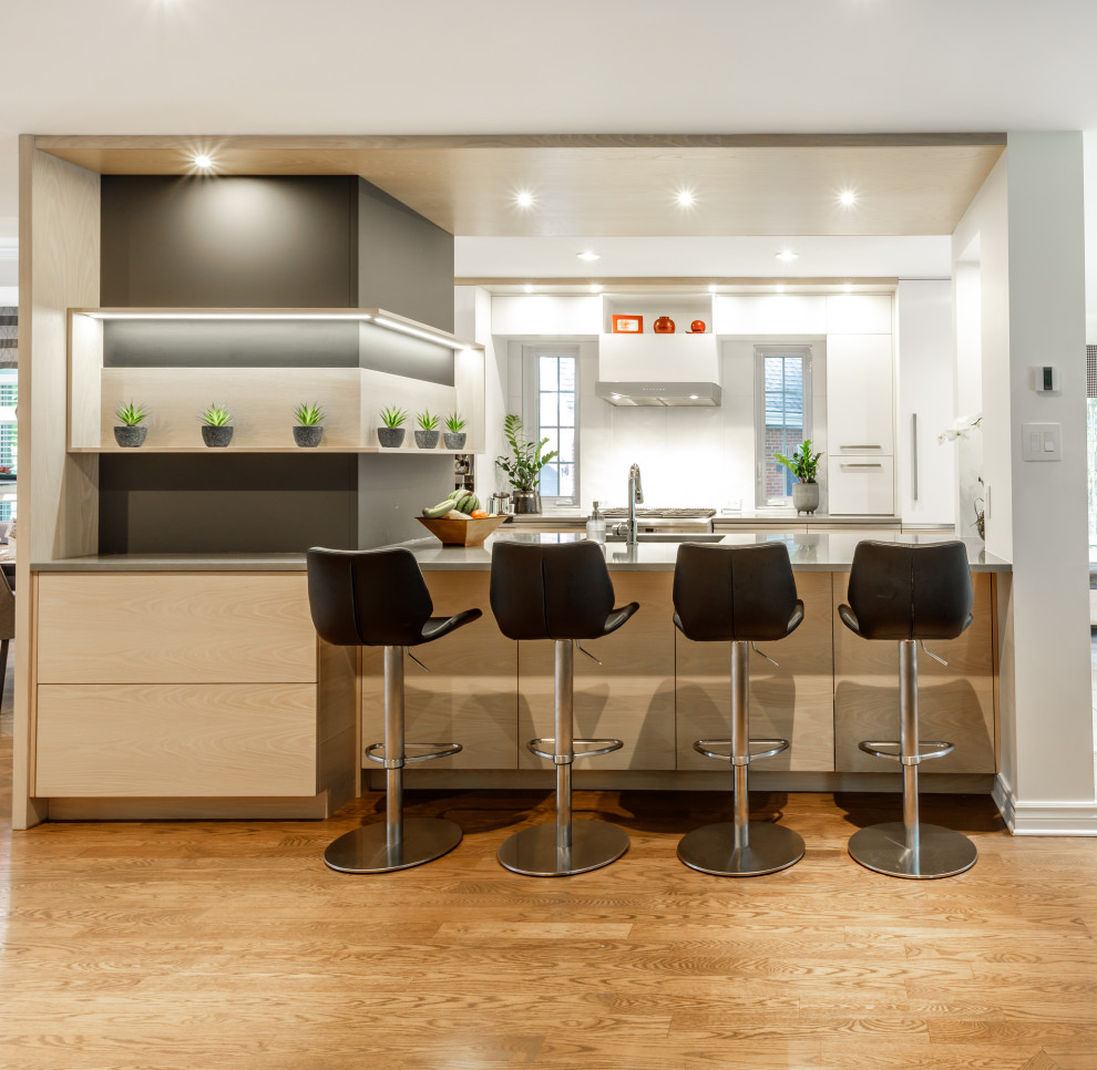 Zweizeilige Moderne Küche mit Unterbauwaschbecken, flächenbündigen Schrankfronten, weißen Schränken, Küchengeräten aus Edelstahl, braunem Holzboden, Kücheninsel, braunem Boden und grauer Arbeitsplatte in Montreal
