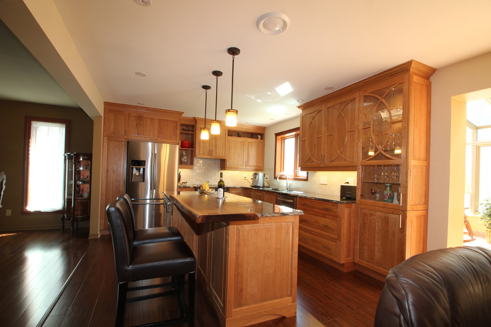 Example of a mid-sized classic l-shaped dark wood floor kitchen design in Montreal with an undermount sink, raised-panel cabinets, medium tone wood cabinets, granite countertops, white backsplash, ceramic backsplash, stainless steel appliances and an island