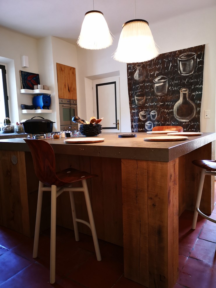 Cette image montre une petite cuisine ouverte rustique en L et bois clair avec un évier intégré, un plan de travail en granite, un électroménager en acier inoxydable, tomettes au sol, îlot, un sol rose et un plan de travail gris.