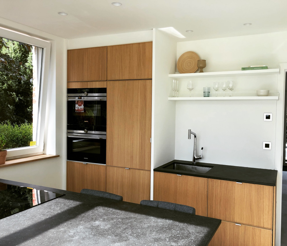 Foto på ett mellanstort medelhavsstil grå kök, med en undermonterad diskho, skåp i ljust trä, bänkskiva i kvarts, vitt stänkskydd, svarta vitvaror, klinkergolv i keramik, en köksö och beiget golv