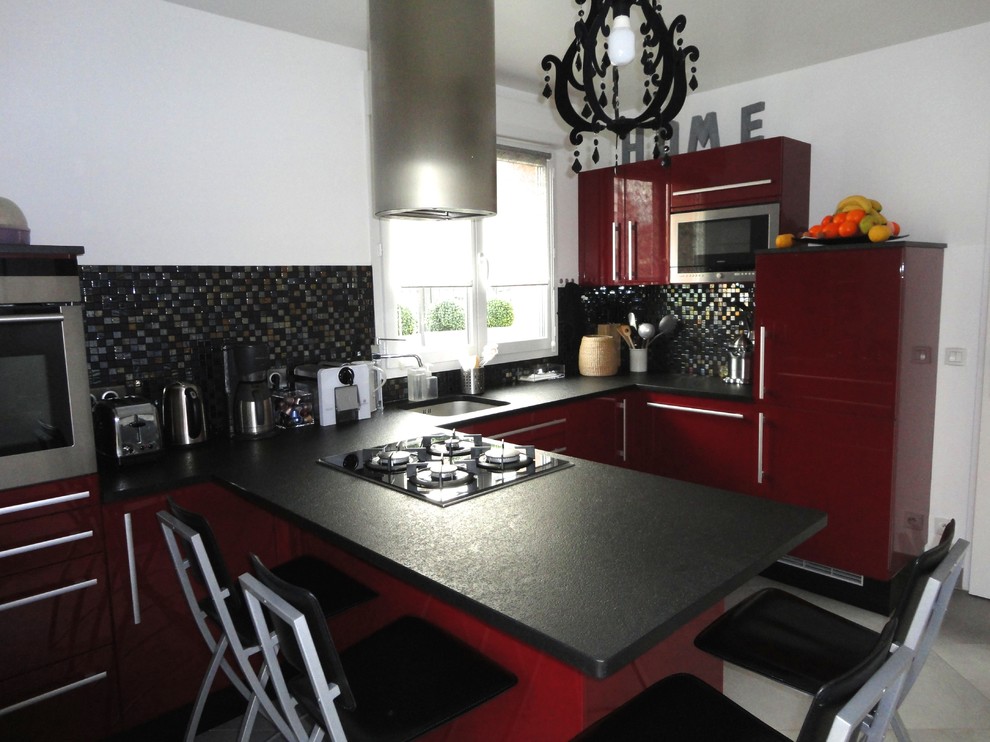 Foto på ett mellanstort, avskilt funkis svart u-kök, med en enkel diskho, släta luckor, röda skåp, granitbänkskiva, stänkskydd i mosaik, rostfria vitvaror, betonggolv, en köksö, svart stänkskydd och grått golv