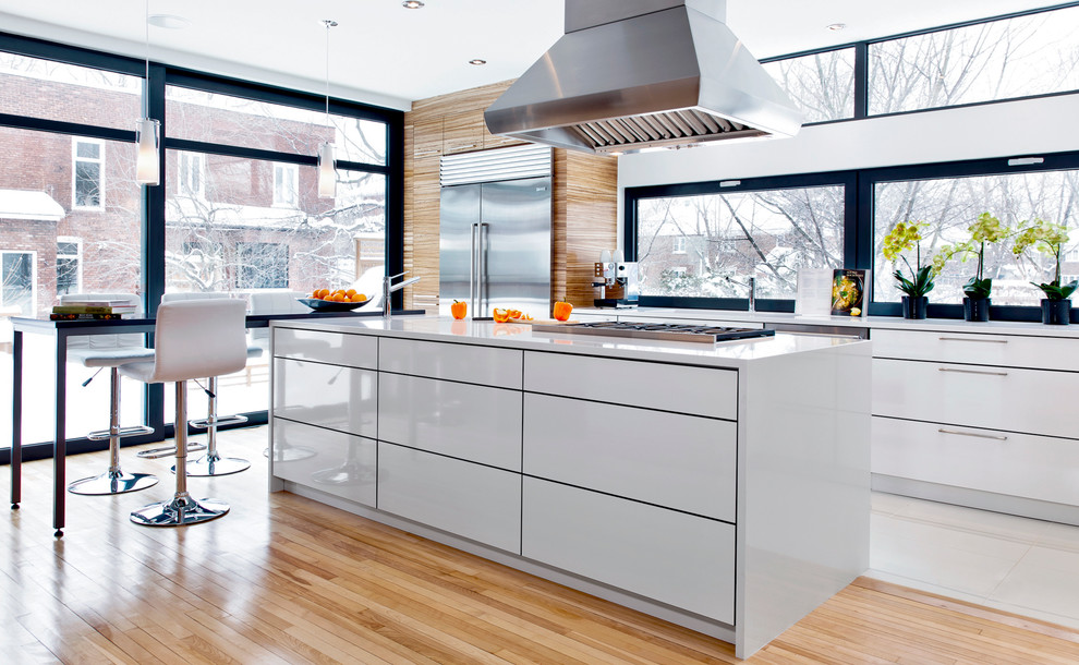 Photo of a contemporary kitchen/diner in Montreal with flat-panel cabinets, white cabinets, stainless steel appliances, medium hardwood flooring and an island.