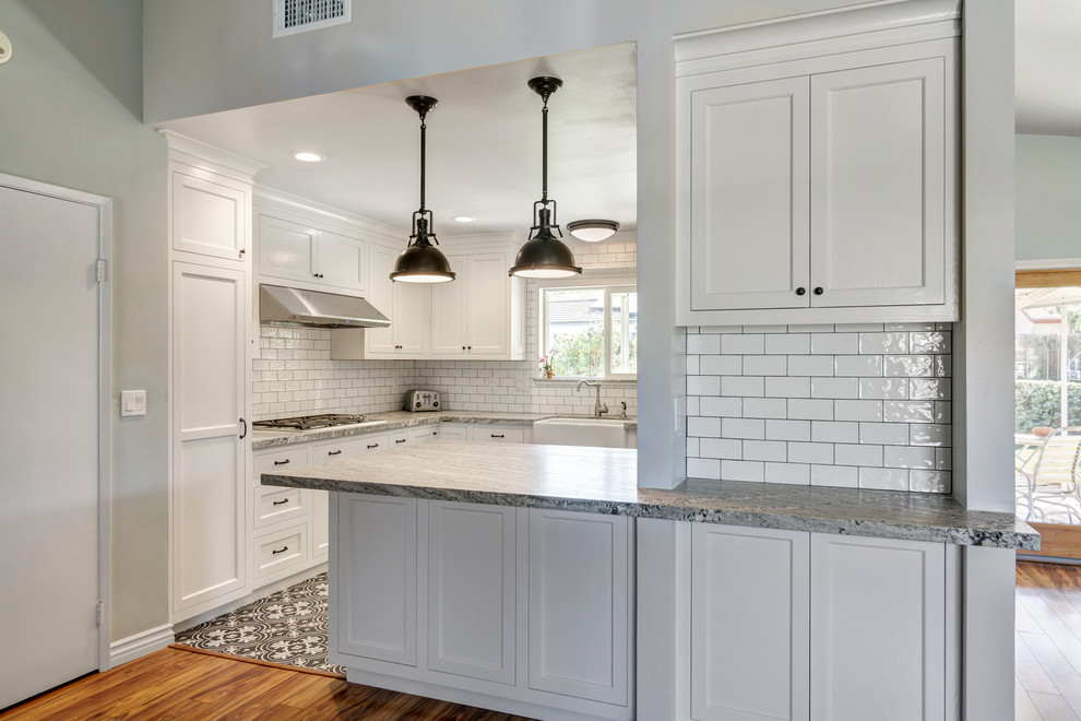 This is an example of a small country galley kitchen pantry in San Diego with a belfast sink, shaker cabinets, white cabinets, granite worktops, white splashback, porcelain splashback, stainless steel appliances, ceramic flooring and a breakfast bar.