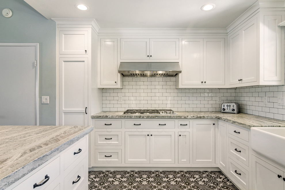 Kitchen pantry - small country galley ceramic tile kitchen pantry idea in San Diego with a farmhouse sink, shaker cabinets, white cabinets, granite countertops, white backsplash, porcelain backsplash, stainless steel appliances and a peninsula