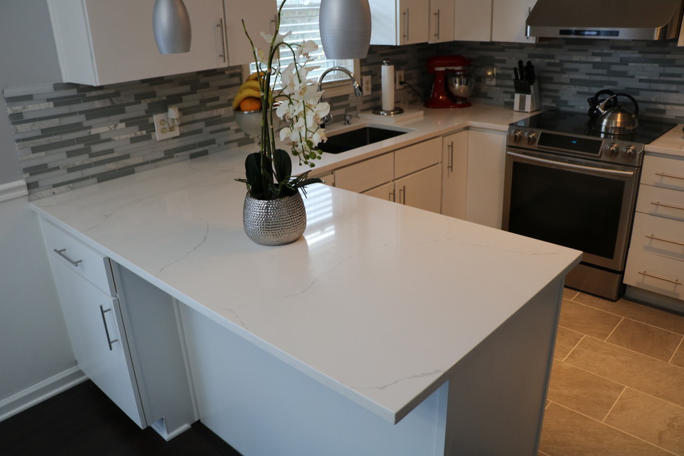 Inspiration for a small contemporary u-shaped kitchen in Grand Rapids with a submerged sink, flat-panel cabinets, white cabinets, quartz worktops, grey splashback, matchstick tiled splashback, stainless steel appliances, porcelain flooring, a breakfast bar and brown floors.