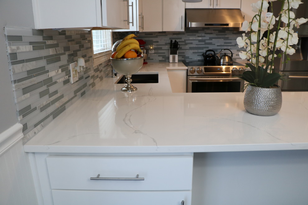 Exempel på ett litet modernt u-kök, med en undermonterad diskho, släta luckor, vita skåp, bänkskiva i kvartsit, grått stänkskydd, stänkskydd i stickkakel, rostfria vitvaror, klinkergolv i porslin, en halv köksö och brunt golv