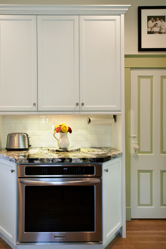 Bild på ett litet vintage kök, med en enkel diskho, luckor med infälld panel, vita skåp, marmorbänkskiva, vitt stänkskydd, stänkskydd i keramik, rostfria vitvaror, mellanmörkt trägolv och en halv köksö