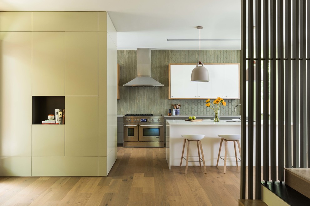 Inspiration for a large contemporary l-shaped open plan kitchen in Austin with a submerged sink, flat-panel cabinets, white cabinets, green splashback, medium hardwood flooring, an island, brown floors, white worktops, engineered stone countertops, ceramic splashback and stainless steel appliances.