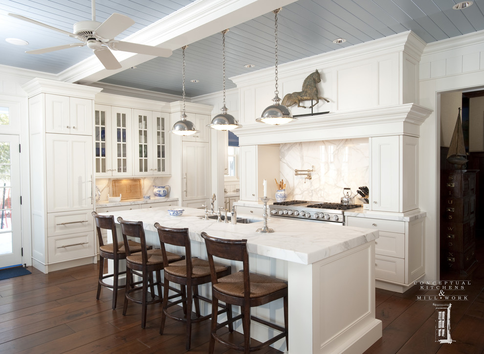 Klassisk inredning av ett kök, med en dubbel diskho, luckor med infälld panel, vita skåp, vitt stänkskydd, rostfria vitvaror, mörkt trägolv och brunt golv
