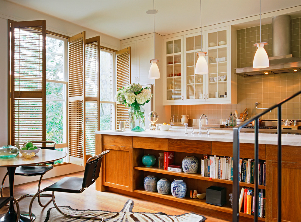 На фото: кухня в современном стиле с стеклянными фасадами, белыми фасадами и зеленым фартуком