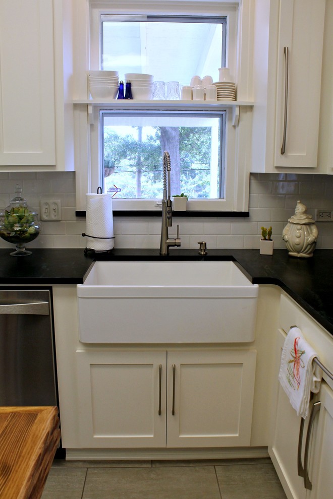 Photo of a small farmhouse l-shaped enclosed kitchen in New Orleans with a belfast sink, shaker cabinets, white cabinets, soapstone worktops, white splashback, metro tiled splashback, stainless steel appliances, ceramic flooring, an island and grey floors.