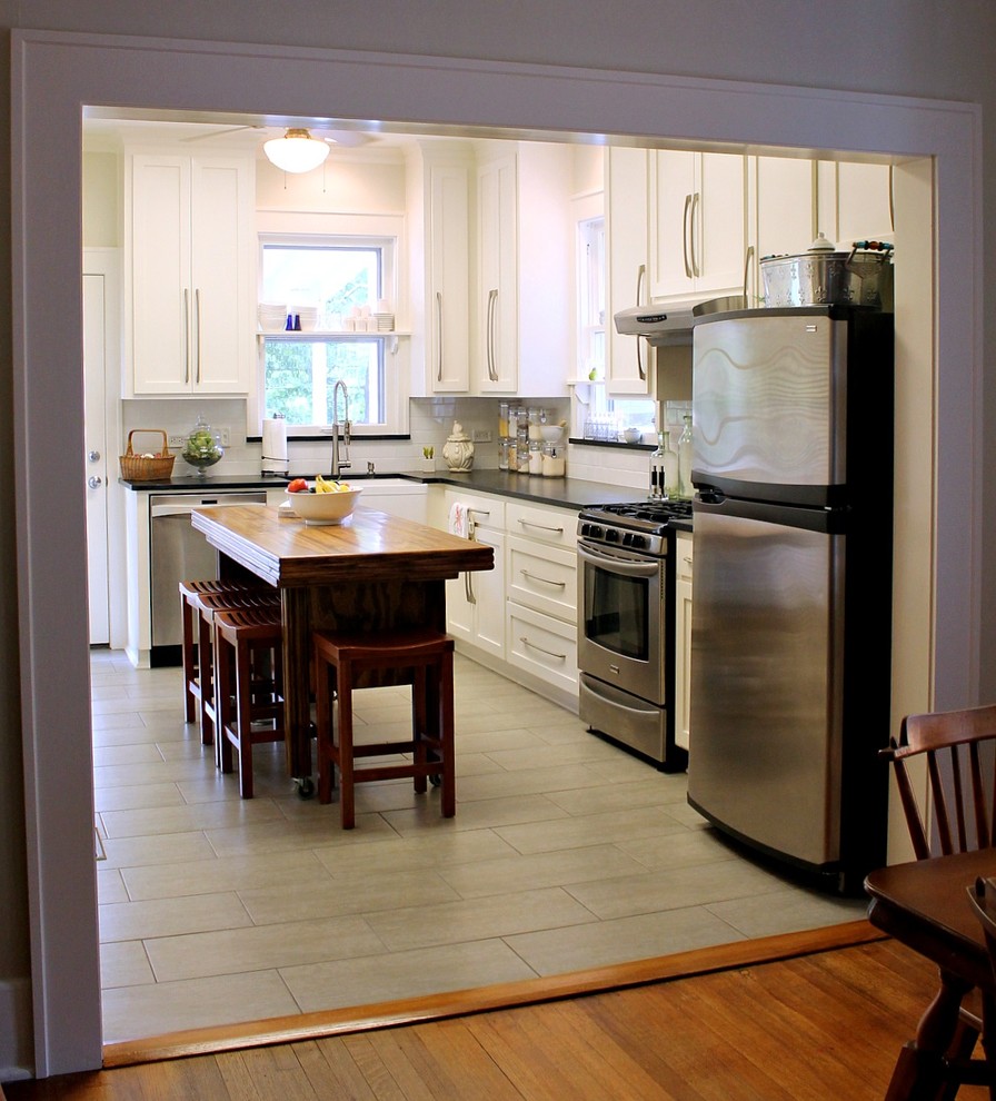 Bild på ett avskilt, litet lantligt l-kök, med en rustik diskho, skåp i shakerstil, vita skåp, bänkskiva i täljsten, vitt stänkskydd, stänkskydd i tunnelbanekakel, rostfria vitvaror, klinkergolv i keramik, en köksö och grått golv
