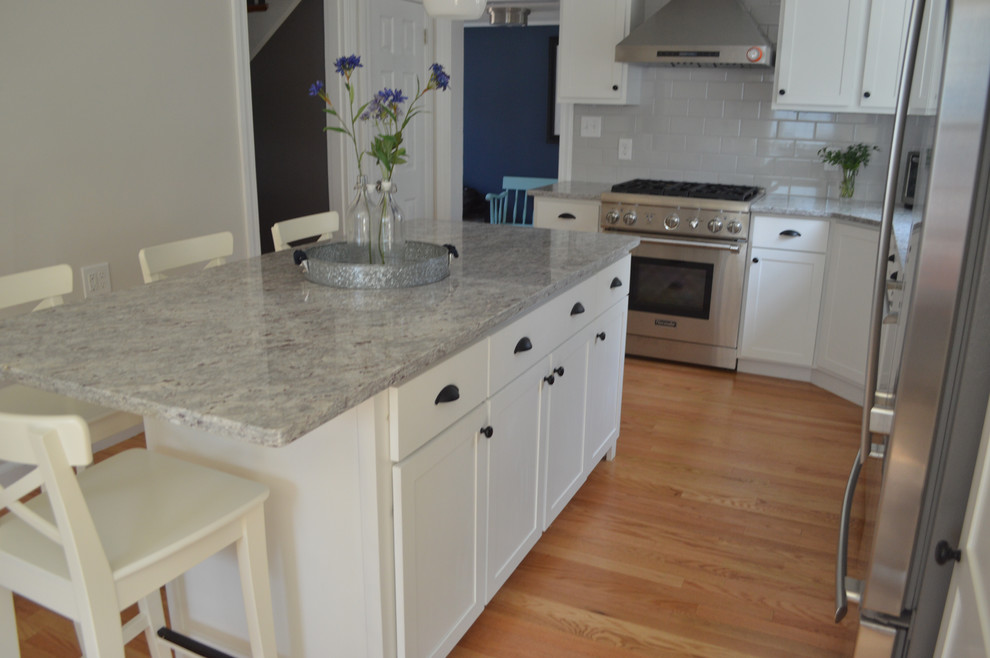 Example of a mid-sized transitional l-shaped light wood floor eat-in kitchen design in Boston with an undermount sink, shaker cabinets, white cabinets, granite countertops, gray backsplash, subway tile backsplash, stainless steel appliances and an island