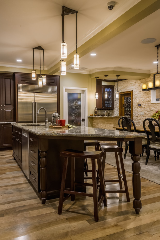 Exemple d'une cuisine américaine chic en L et bois foncé de taille moyenne avec un placard avec porte à panneau surélevé, un plan de travail en granite, un électroménager en acier inoxydable, un sol en bois brun, îlot et un sol marron.