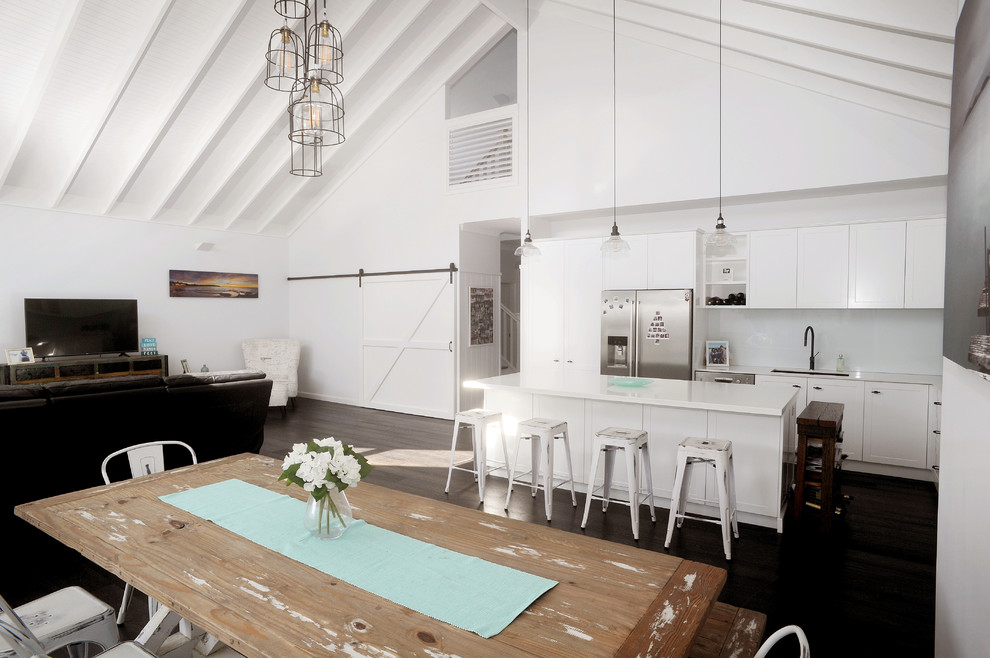 Idéer för ett stort maritimt vit kök, med en dubbel diskho, vita skåp, vitt stänkskydd, glaspanel som stänkskydd, rostfria vitvaror, mörkt trägolv och en köksö