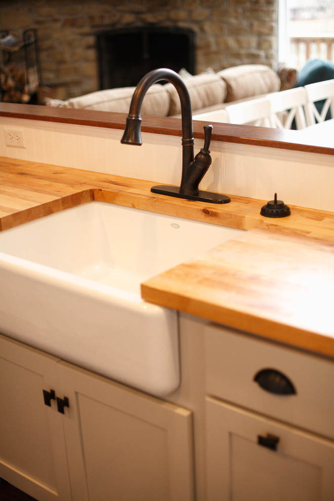 Lantlig inredning av ett mellanstort kök, med en rustik diskho, skåp i shakerstil, vita skåp, träbänkskiva, vitt stänkskydd, stänkskydd i trä, vita vitvaror, mörkt trägolv, en halv köksö och brunt golv