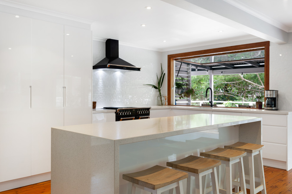 Photo of a large contemporary l-shaped kitchen/diner in Gold Coast - Tweed with flat-panel cabinets, white cabinets, engineered stone countertops, white splashback, mosaic tiled splashback, stainless steel appliances, an island and beige worktops.