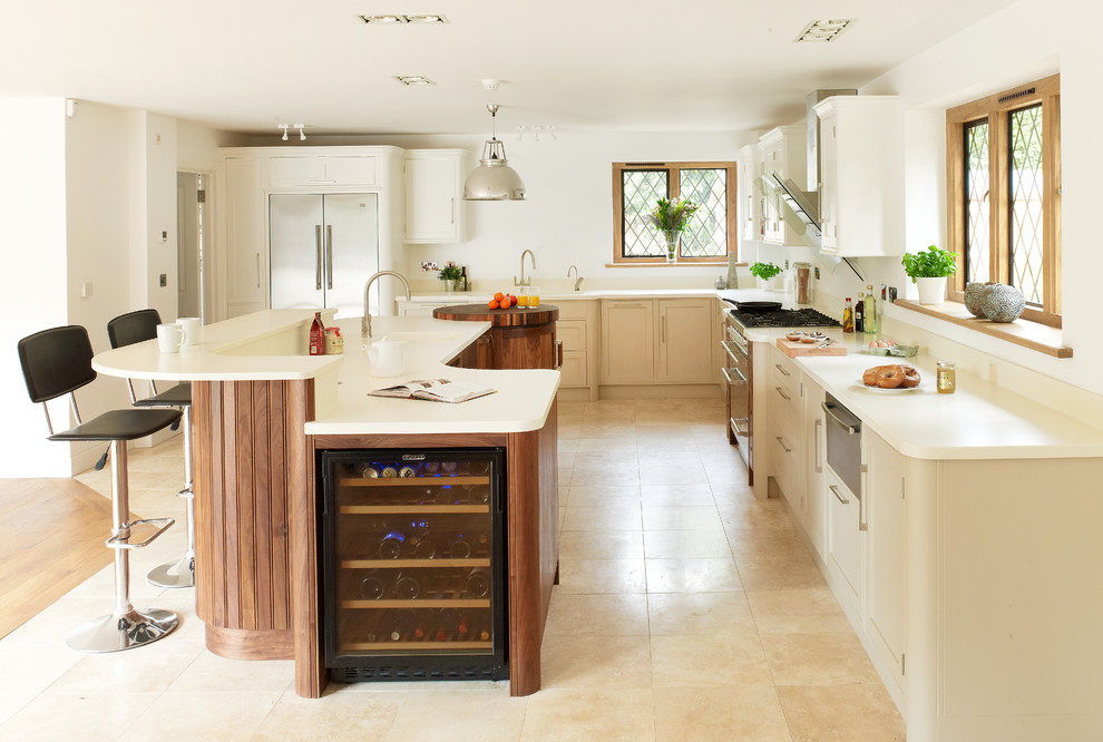Küche in L-Form mit Schrankfronten im Shaker-Stil, weißen Schränken, Küchengeräten aus Edelstahl, Travertin und Kücheninsel in Kent