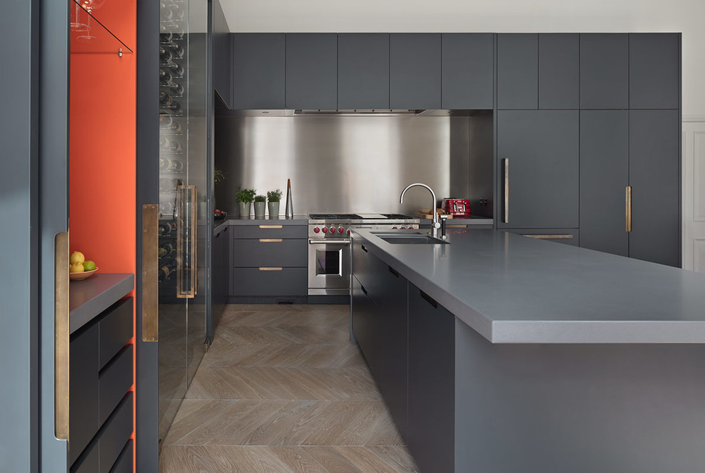 Expansive contemporary galley open plan kitchen in London with a submerged sink, glass-front cabinets, grey cabinets, composite countertops, light hardwood flooring, an island, brown floors and grey worktops.