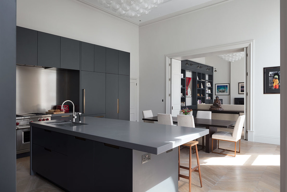 Expansive contemporary galley open plan kitchen in London with a submerged sink, glass-front cabinets, grey cabinets, composite countertops, light hardwood flooring, an island, brown floors and grey worktops.