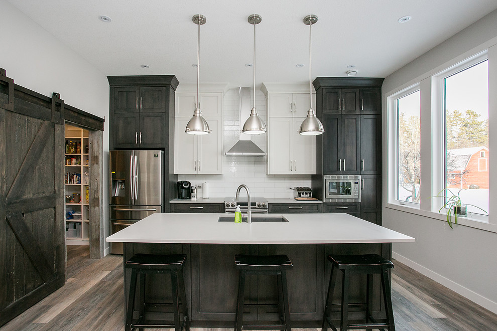 Traditional kitchen in Calgary with a submerged sink, shaker cabinets, dark wood cabinets, white splashback, stainless steel appliances, medium hardwood flooring and an island.