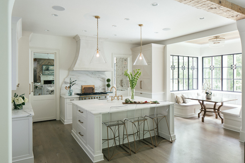 Design ideas for a large classic l-shaped kitchen/diner in Atlanta with a belfast sink, shaker cabinets, white cabinets, marble worktops, white splashback, marble splashback, stainless steel appliances, dark hardwood flooring, an island and brown floors.