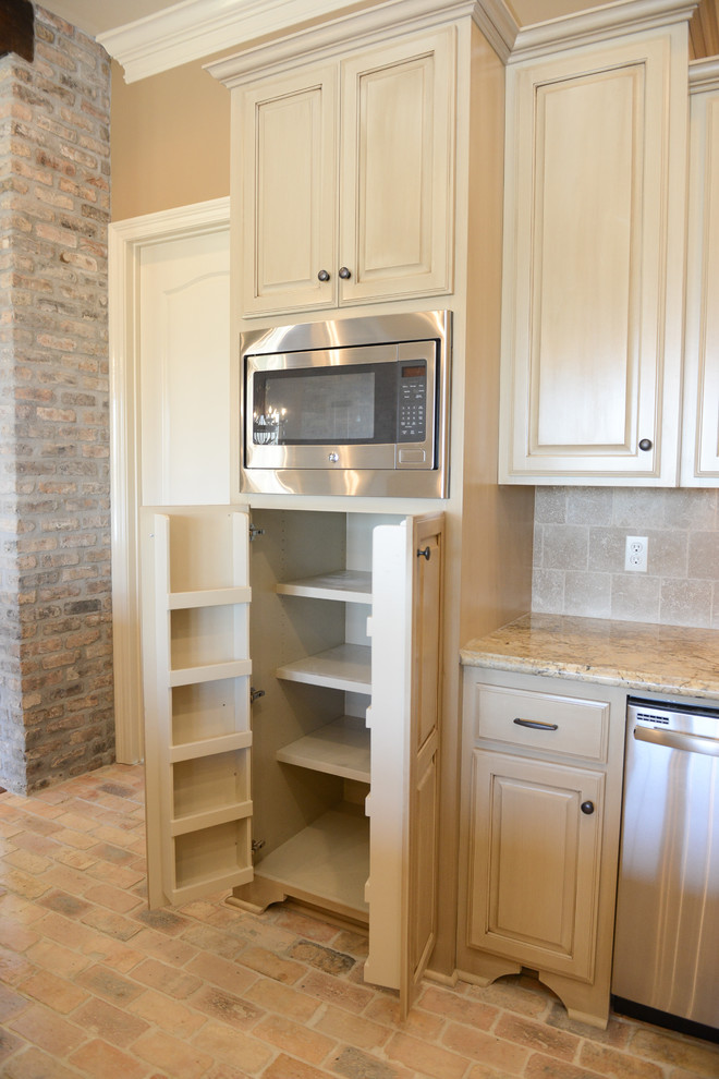 Klassisk inredning av ett mellanstort beige beige kök, med en undermonterad diskho, luckor med upphöjd panel, beige skåp, granitbänkskiva, beige stänkskydd, stänkskydd i stenkakel, rostfria vitvaror, tegelgolv, en köksö och flerfärgat golv