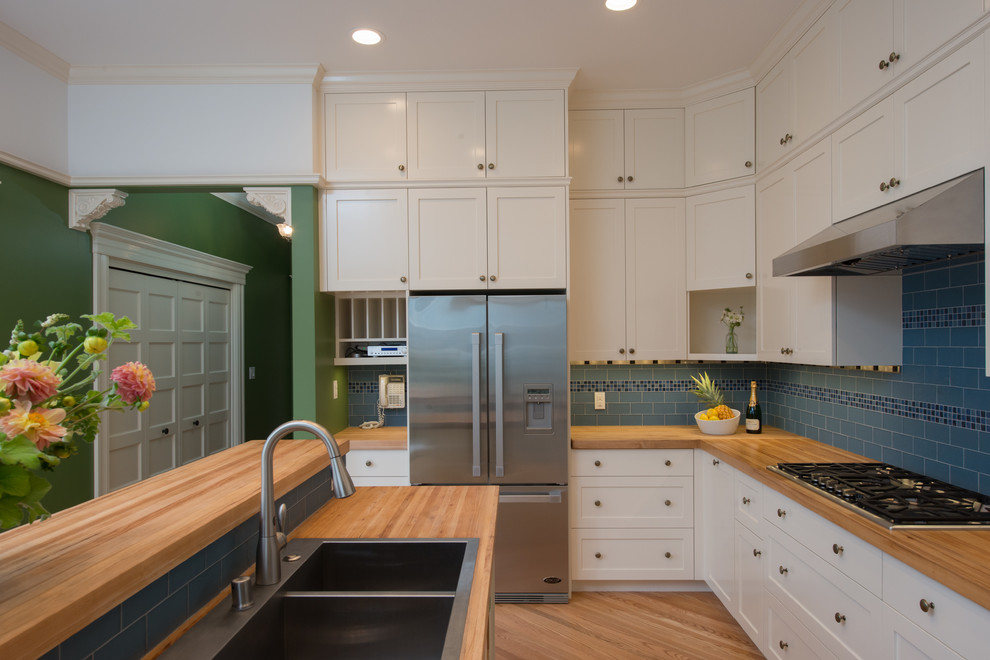 Geschlossene Klassische Küche mit Doppelwaschbecken, Schrankfronten im Shaker-Stil, weißen Schränken, Arbeitsplatte aus Holz, Küchengeräten aus Edelstahl, braunem Holzboden und Kücheninsel in San Francisco