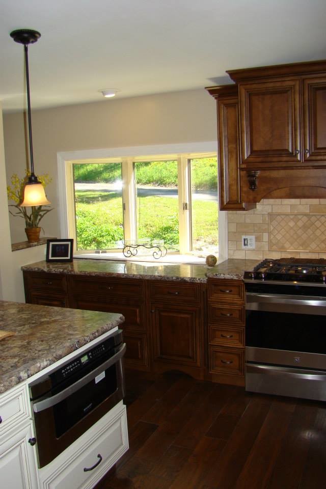 Amerikansk inredning av ett stort kök, med en dubbel diskho, luckor med upphöjd panel, beige stänkskydd, stänkskydd i keramik, rostfria vitvaror, en köksö, skåp i mörkt trä, granitbänkskiva, mörkt trägolv och brunt golv