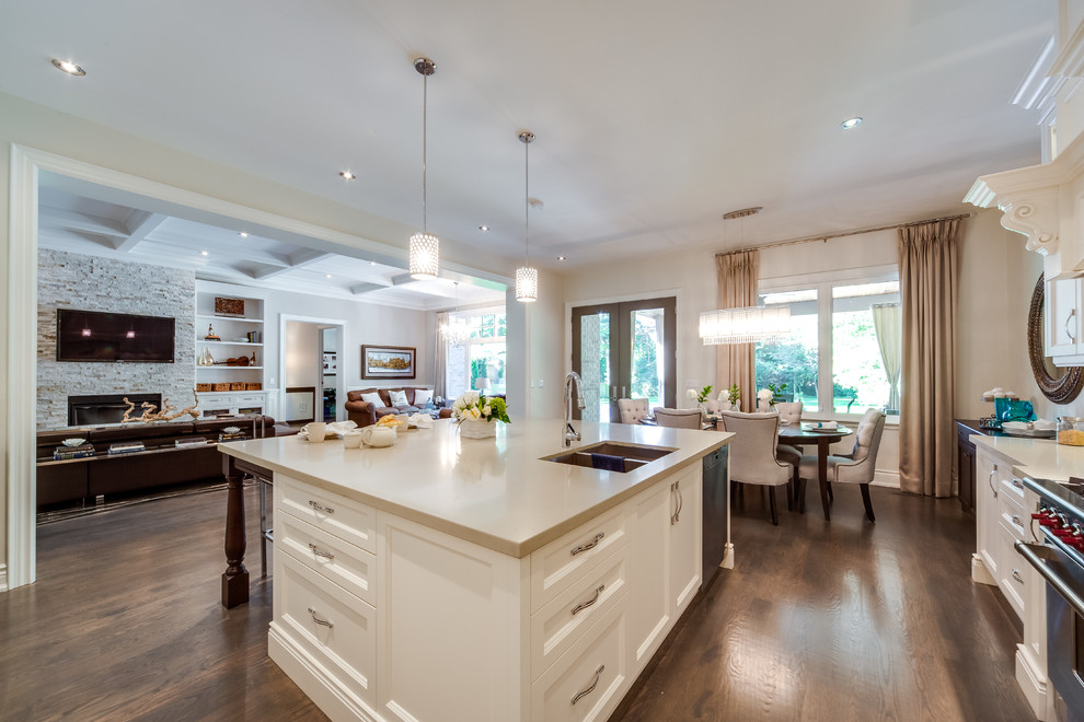 Large traditional l-shaped open plan kitchen in Toronto with a double-bowl sink, recessed-panel cabinets, white cabinets, quartz worktops, grey splashback, mosaic tiled splashback, integrated appliances, dark hardwood flooring, an island and brown floors.