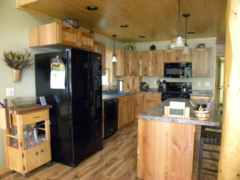 Example of a mid-sized classic l-shaped medium tone wood floor and brown floor open concept kitchen design in Other with a drop-in sink, recessed-panel cabinets, light wood cabinets, granite countertops, black appliances and an island