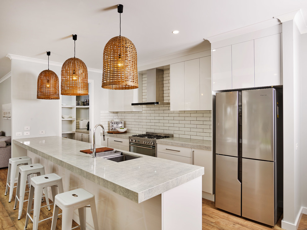 Inspiration for a mid-sized contemporary galley laminate floor and brown floor kitchen remodel in Other with an undermount sink, flat-panel cabinets, white cabinets, quartz countertops, white backsplash, subway tile backsplash, stainless steel appliances, an island and gray countertops